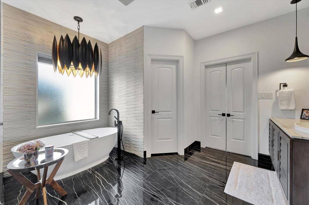 The primary ensuite features designer lighting that illuminates the luxurious soaker tub, beautifully surrounded by bamboo-inspired wall treatments. The porcelain tile floor, named Thunder Night, enhances the serene ambiance with its deep, rich tones, creating a harmonious and sophisticated space.