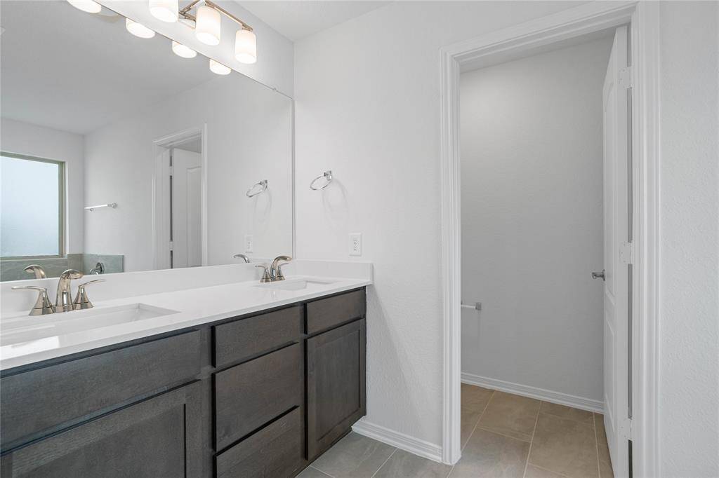 This primary bathroom is definitely move-in ready! Featuring stained cabinets with light countertops and dual sinks, Moen faucets, mirror, lighting, high ceilings, neutral paint, tile flooring, and toilet compartment.