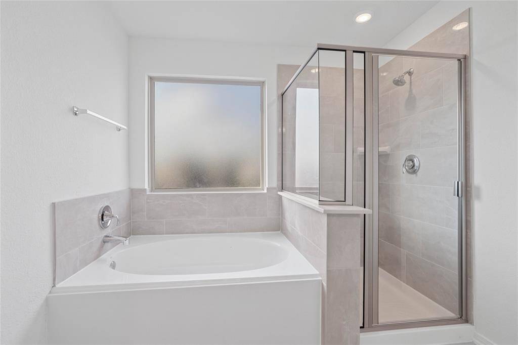 Additional view of the primary bathroom features a walk-in shower with tile surround, garden tub with custom tile, Moen faucets, and an obscure window bringing in natural lighting.