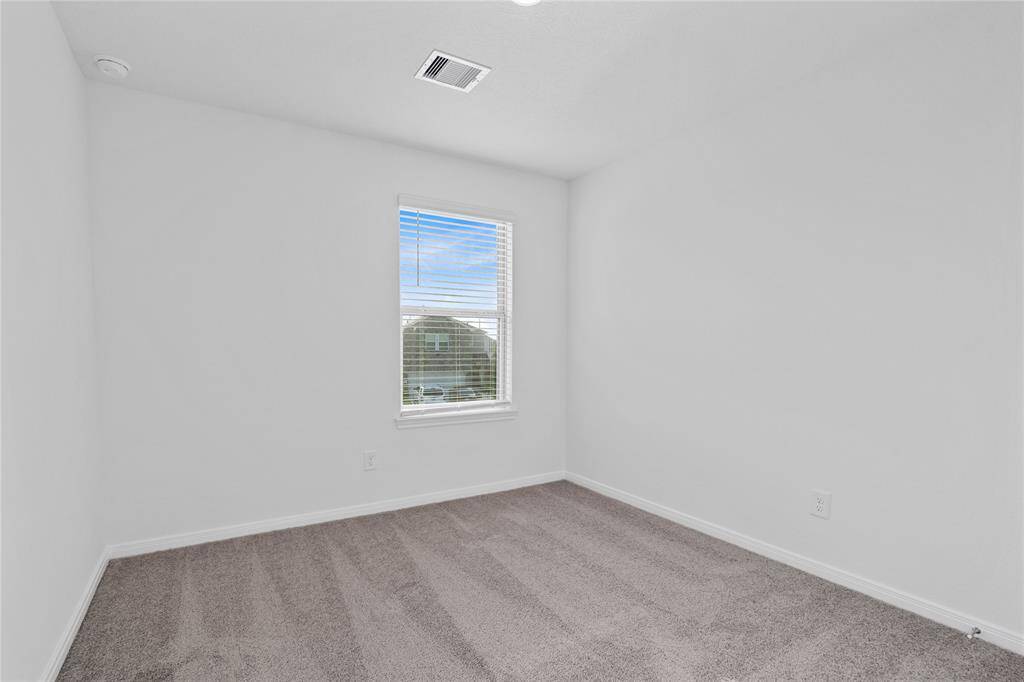 Secondary bedroom features plush carpet, neutral paint, lighting, ample closet space, and a large window with blinds.