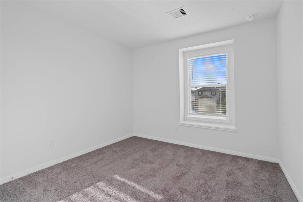 Secondary bedroom features plush carpet, neutral paint, lighting, ample closet space, and a large window with blinds.