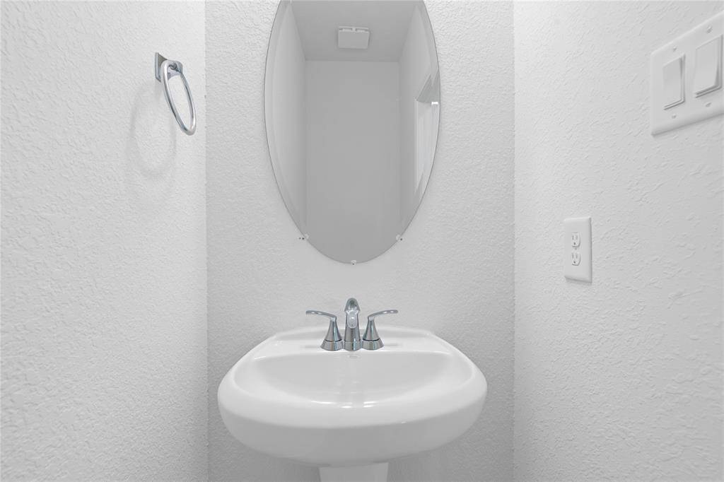 Powder room on the first floor features pedestal sink with Moen Seena Bathroom Faucet, oval mirror, toilet, custom paint and vinyl plank flooring.