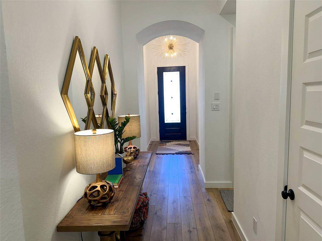 Welcome home to this inviting entryway, featuring sleek wood look luxury vinyl plank flooring that extends throughout the hall, guiding you into the heart of the home. The high ceilings and custom chandelier lighting add a touch of sophistication. Creating a warm and welcoming atmosphere from the moment you step inside. The modern front door allows light to flow through.