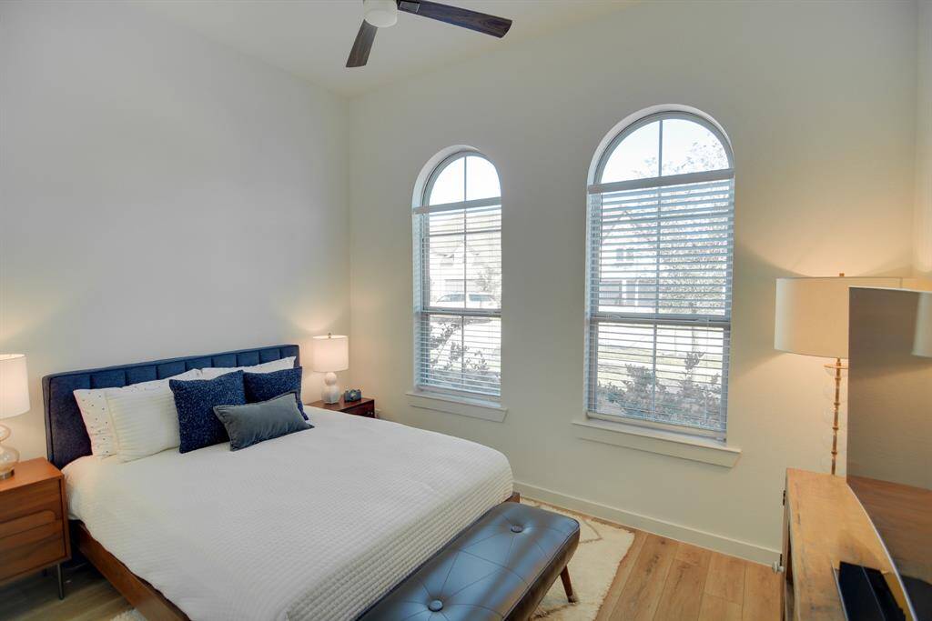 Secondary bedroom features wood look luxury vinyl plank flooring, neutral paint, modern ceiling fan with lighting and large windows with privacy blinds.