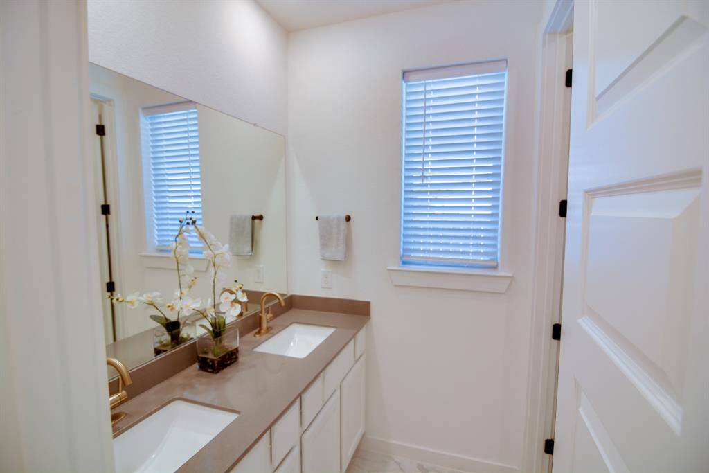 Secondary bath features tile flooring, light cabinets, beautiful dark countertops, mirror, double sinks, gold sleek fixtures and modern finishes.