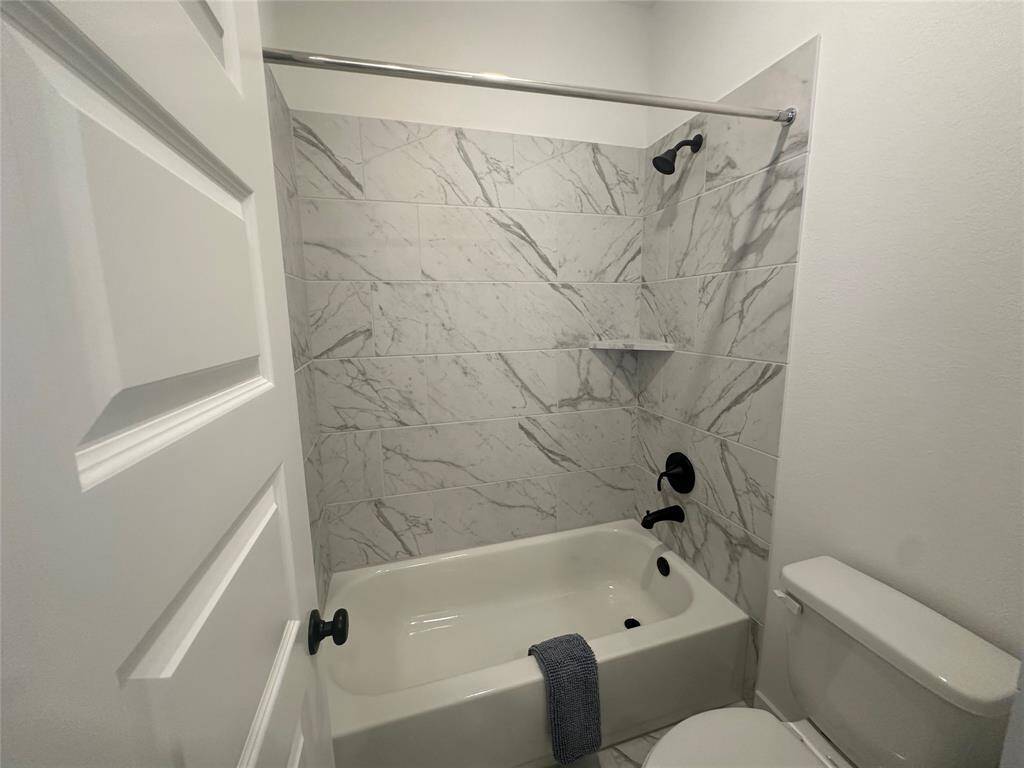 Secondary bath/shower combo with tile surround and tile flooring.
