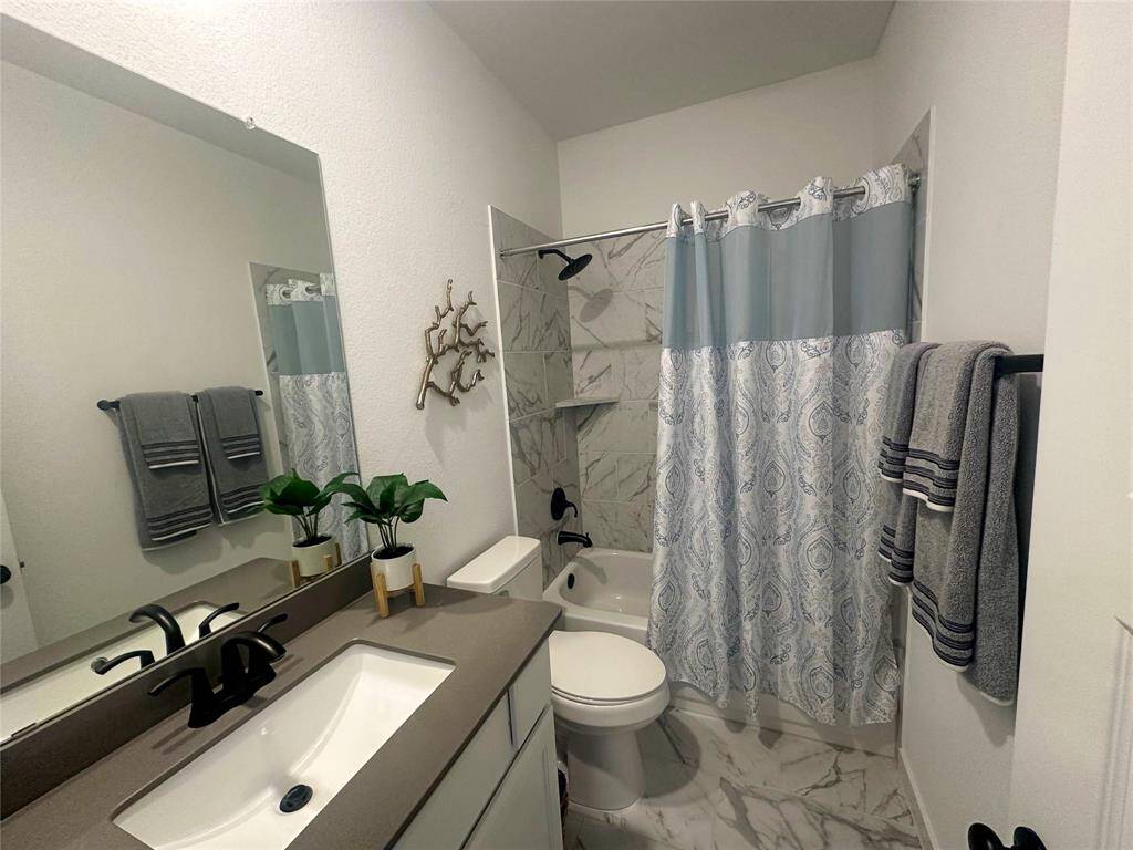 Secondary bathroom located in the secondary bedroom, features dark countertops and cabinets, custom paint, large soaking tub with shower, tile surround, mirror, tile floors, sleek fixtures and modern finishes. Plenty of space to accommodate any visiting family or guests.