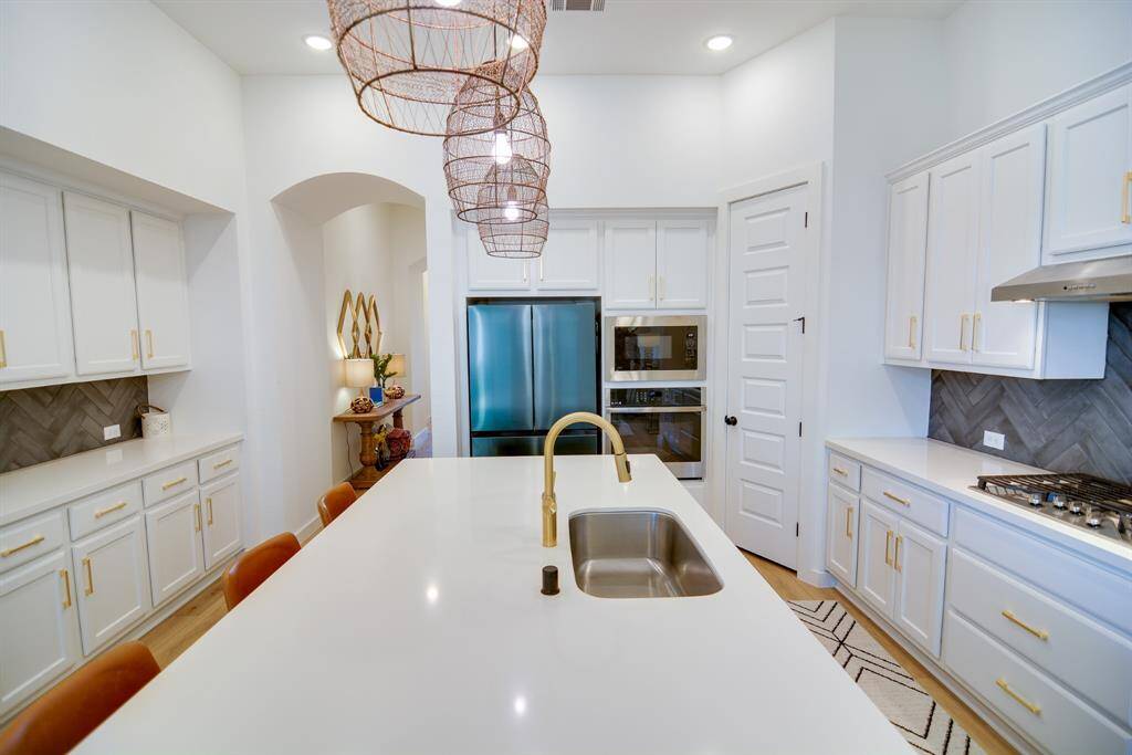 The custom cabinets and gold hardware offer a stylish display and convenient storage, perfect for entertaining. Enjoy the sleek gas cooktop and ample prep space on the beautifully veined countertops, ideal for creating culinary masterpieces. This kitchen seamlessly blends functionality with sophistication, making it the heart of the home.
