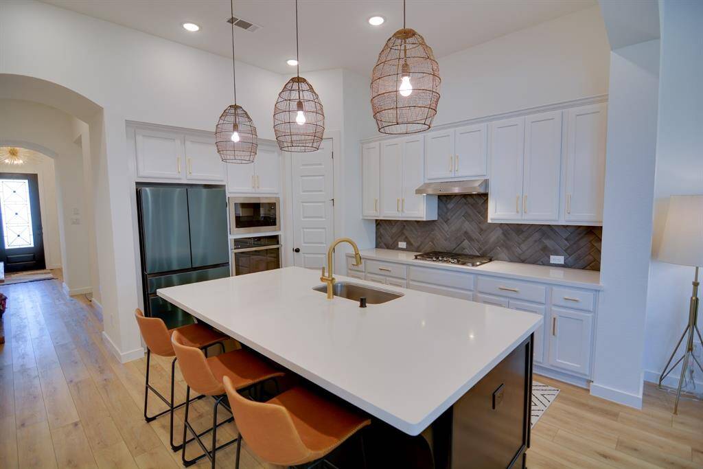This kitchen is by far any chef's dream! This spacious kitchen features wood look luxury vinyl plank flooring, high ceilings, bright wood cabinets, Quartz countertops, Stainless steel appliances, modern tile backsplash, recessed lighting with additional custom pendant lighting, extended counter space, kitchen island with farmhouse sink and space for breakfast bar.