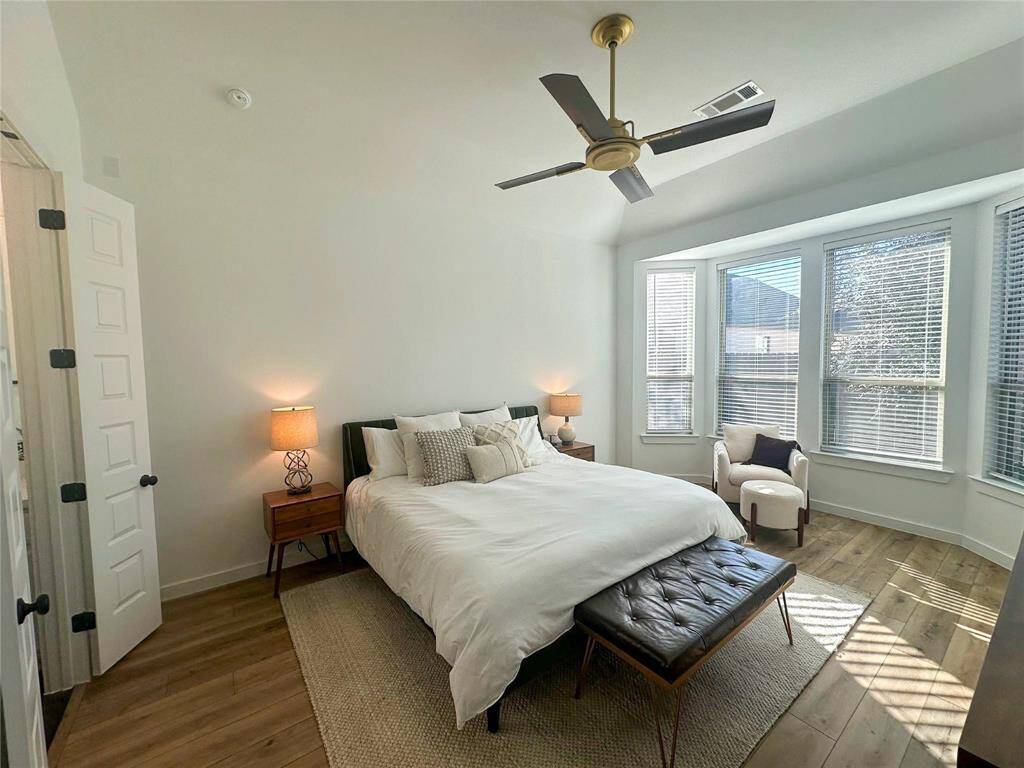What a wonderful place to come home to, this stunning primary suite greets you with wood look luxury vinyl plank flooring, a warm neutral paint, high ceiling, dark stained ceiling fan with gold accents, lovely large windows with blinds allowing in natural light brightening up this spacious primary bedroom, with extra space for a seating area.