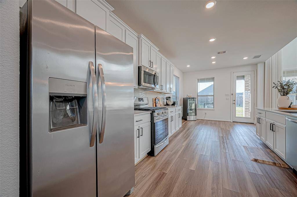 This kitchen features modern stainless steel appliances, sleek white cabinetry, and wood flooring. It has ample natural light and a convenient layout, ideal for cooking and entertaining. (Refrigerator included)