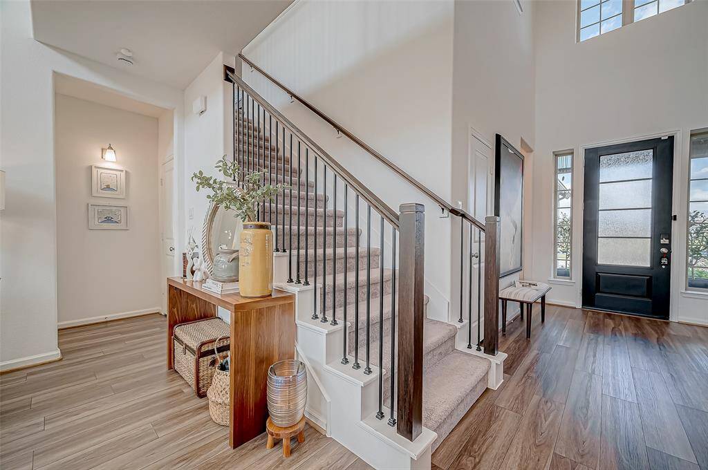 This inviting entryway features a modern staircase with dark wood accents, a stylish table with decorative items, and a large front door with glass panels, all set on elegant laminate flooring.