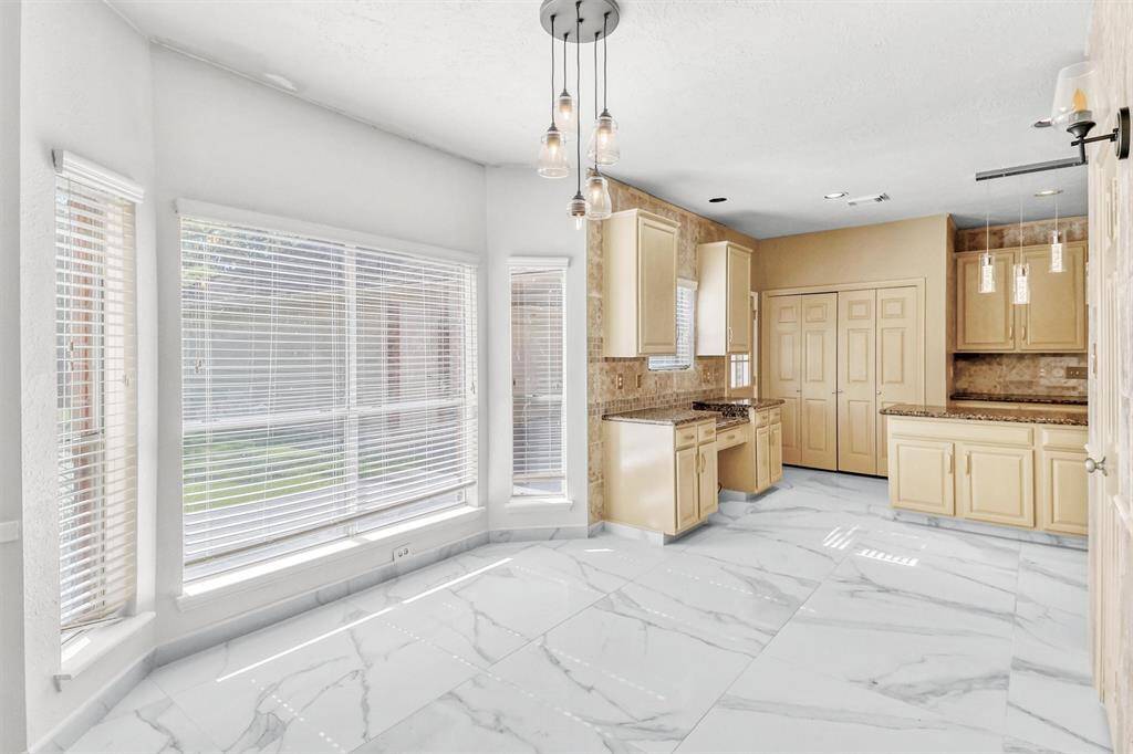 This is a bright, contemporary kitchen with ample natural light, featuring marble flooring, light wood cabinets, and modern lighting fixtures.