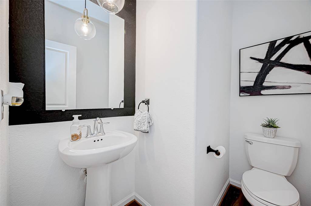 This is a modern half bathroom featuring a pedestal sink, stylish mirror, and contemporary lighting. Decorated wall art, with a clean, minimalist design.