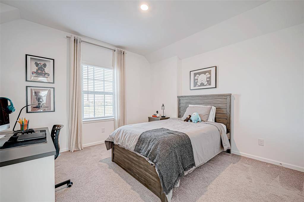 This photo shows a bright, cozy bedroom with neutral walls and carpet. The room features a queen bed with simple linens, a small desk with a chair, and wall art. The window allows for natural light, creating a welcoming atmosphere. ( furniture is not included in the sale)