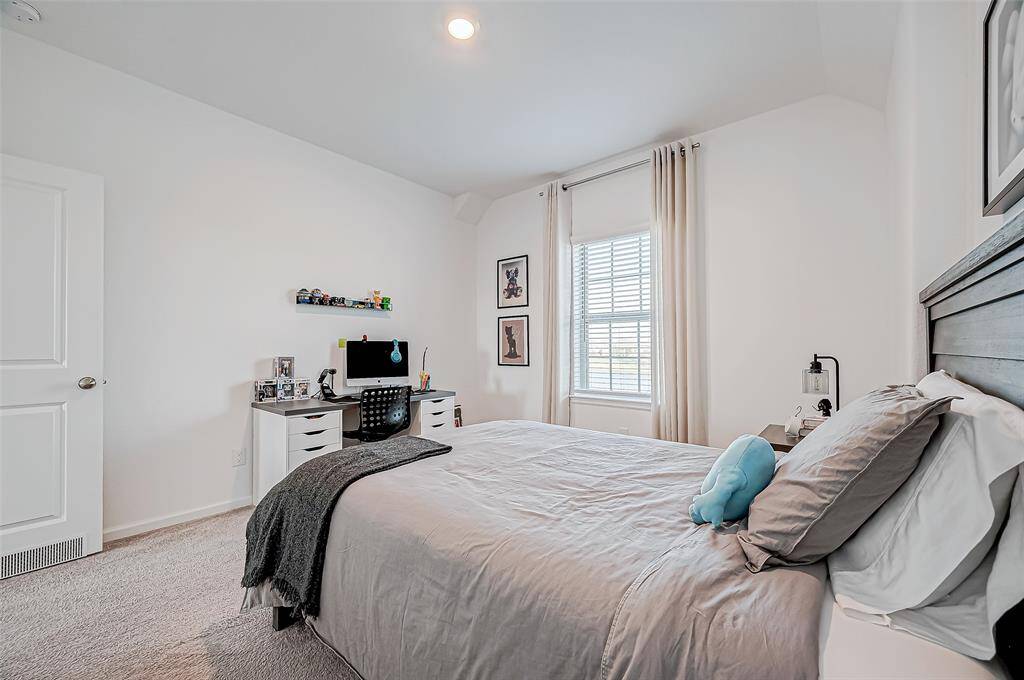 Bright and cozy bedroom with a large window, neutral walls, and plush carpet. Features a comfortable bed, a desk with a computer setup, and stylish decor, creating a welcoming atmosphere.