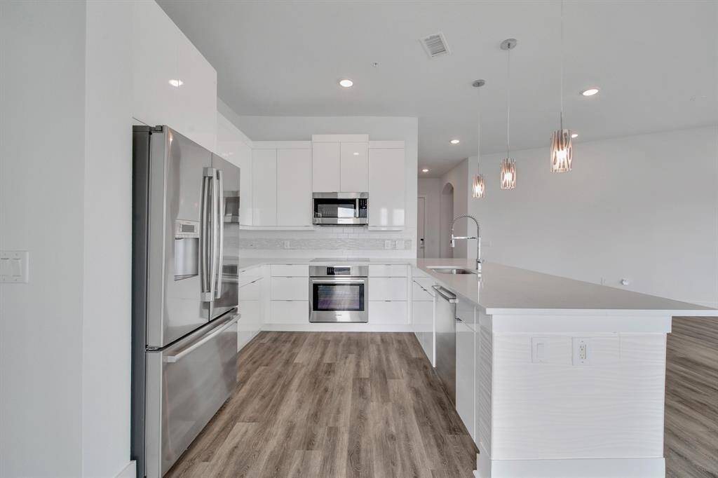 Gorgeous kitchen with stainless steel appliances, white cabinetry, and an island with pendant lighting. Wood-look flooring adds warmth to the sleek design.
