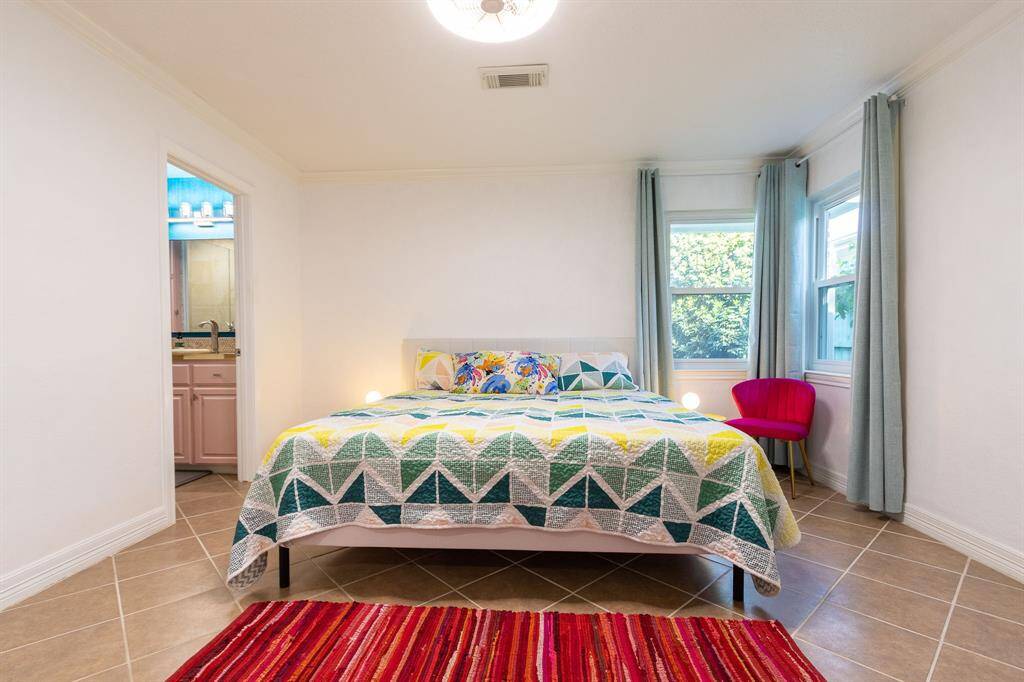 Primary bedroom with king sized bed. Corner windows, crown molding and baseboards. Ensuite bathroom to the left.