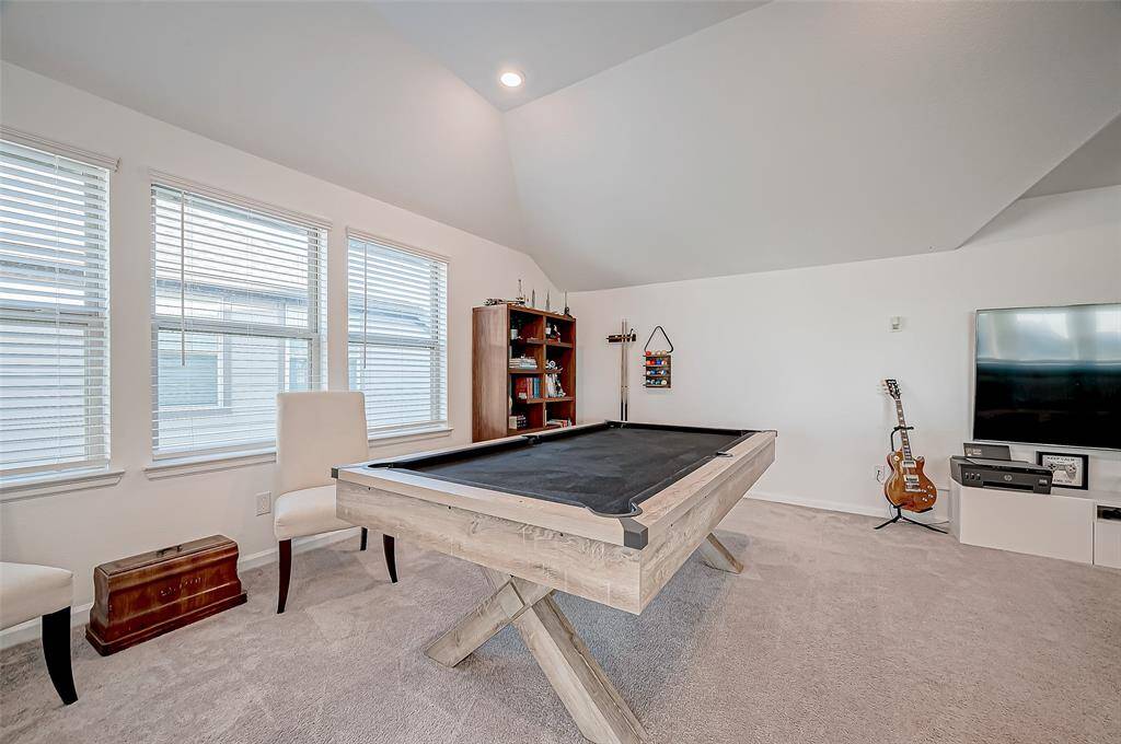 This spacious game room features a modern pool table, cozy carpet, and ample natural light from large windows. The room is stylish entertainment setup with a TV and shelves, offering a perfect space for relaxation and leisure activities. ( All furniture excluded from the sale)