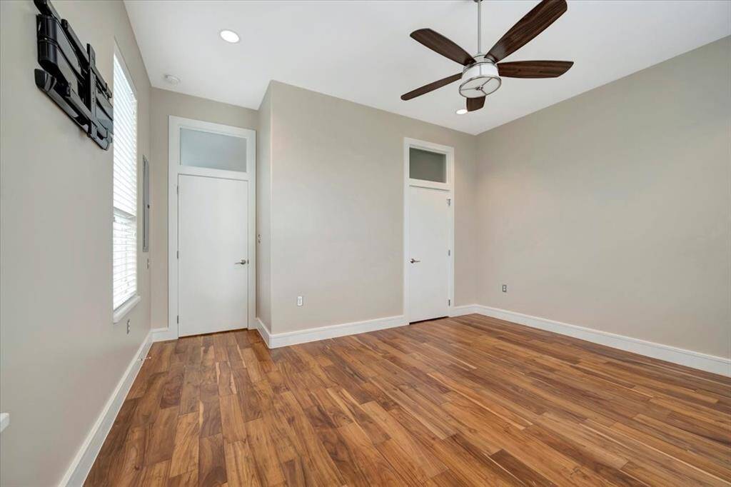 A serene first-floor bedroom featuring rich hardwood floors, two-inch faux blinds for privacy, and large windows offering breathtaking views of the bay.