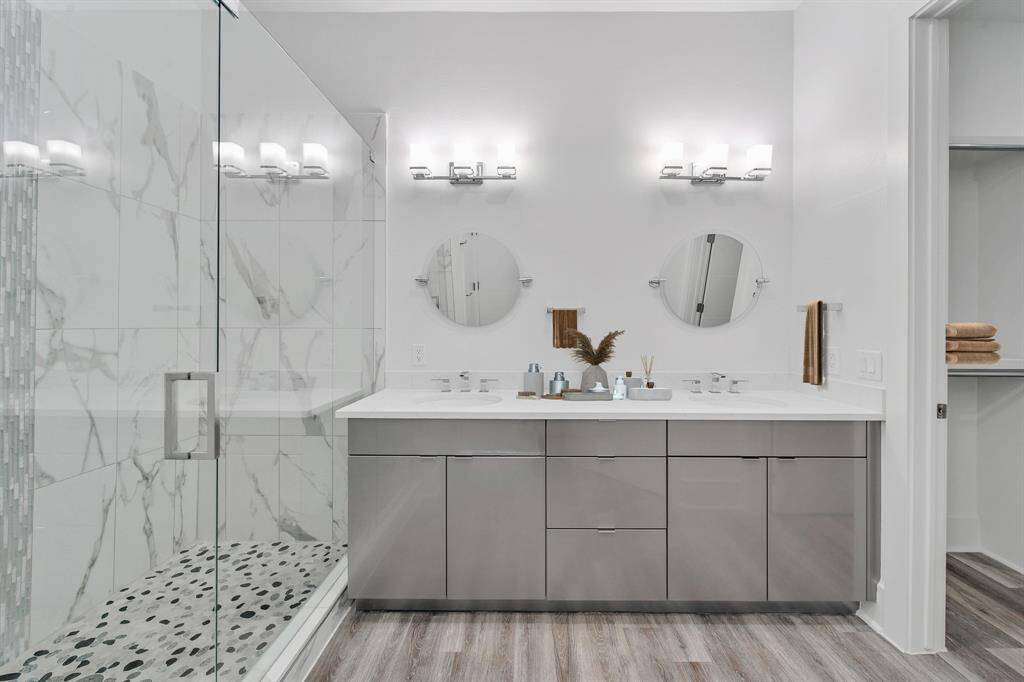 Luxury bathroom featuring a large walk-in shower with marble-like tiles, dual vanity with under-sink storage, two round mirrors, and stylish light fixtures.