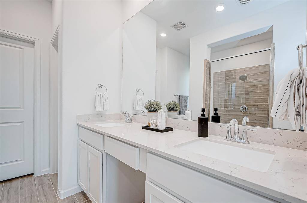 The primary bathroom features a modern design with a double vanity, sleek countertops, and ample storage. It includes a spacious shower with contemporary tile work, and is well-lit with recessed lighting, creating a fresh and inviting atmosphere.