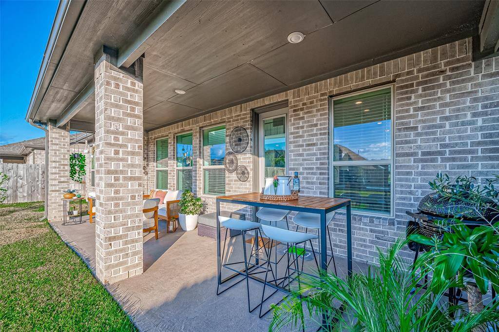 This photo showcases a cozy outdoor patio with brick walls and a covered ceiling. It features a dining area with modern seating, decorative plants, and a relaxed atmosphere perfect for entertaining or enjoying a quiet evening.