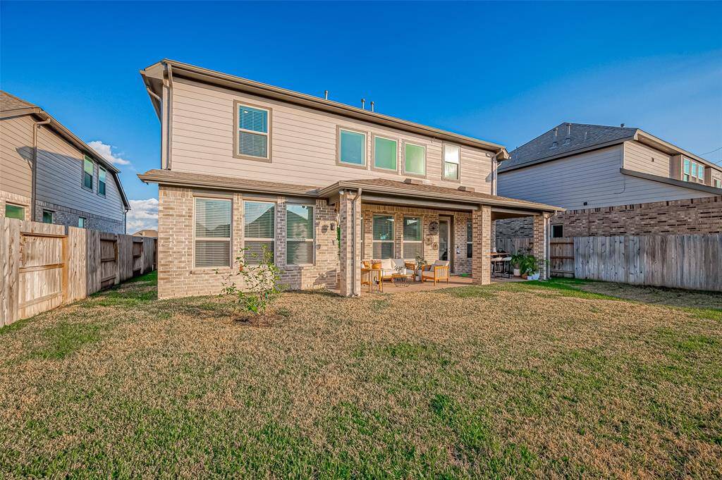 This photo shows a two-story home with a spacious backyard. The house features a covered patio area with seating, ideal for outdoor relaxation. The exterior is a combination of brick and siding, and the yard is fully fenced for privacy. Features Sprinkler System front and back.