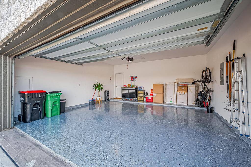 This spacious garage features a sleek, speckled epoxy floor and ample storage space, with neatly organized tools, room for bicycles and shelving. It offers a clean, bright environment perfect for vehicles and additional storage needs.