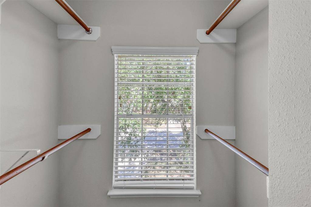 This is a well-lit staircase with wooden handrails on both sides and a large window allowing natural light to come in, which overlooks greenery outside.