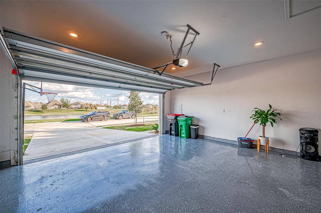 A spacious garage with a polished floor, ample storage space, and direct access to the driveway.  It features an automatic door opener, ceiling lights, and a view of a well-kept neighborhood street and Lake View.