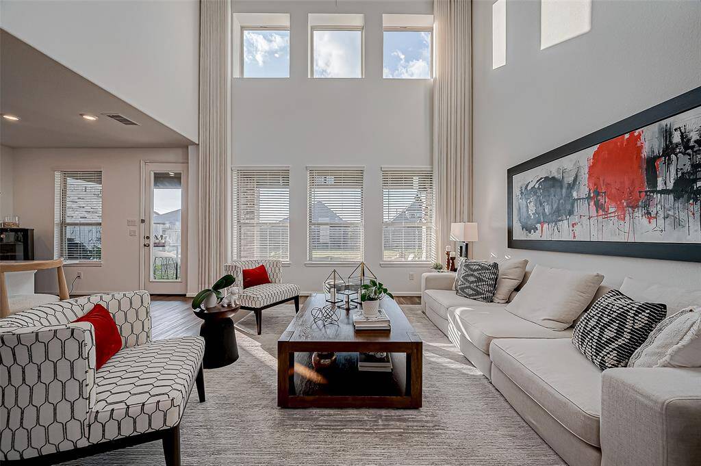 Bright and spacious living room with high ceilings, large windows, and modern decor. Features ample seating, contemporary artwork, and abundant natural light. Custom Curtains and Rods in this photo included with the property.)