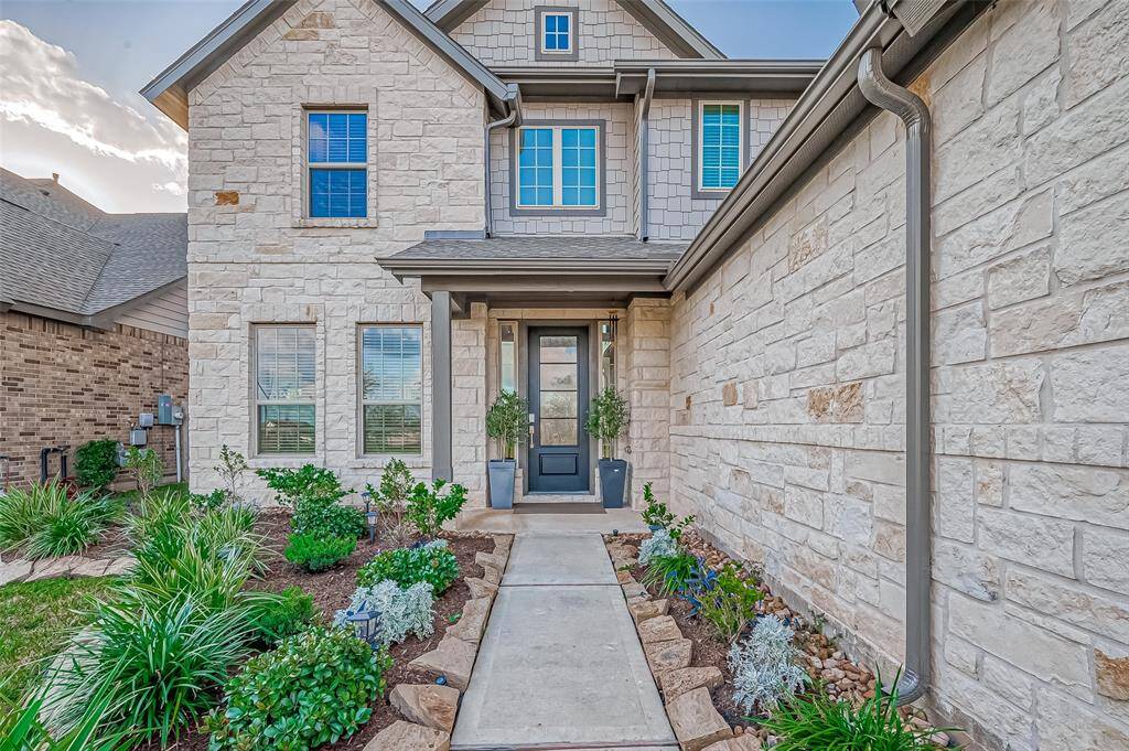 This photo showcases a modern two-story home with a stone exterior. The inviting front entrance features a covered porch and a well-maintained garden lining the walkway. The house has large windows, offering plenty of natural light.