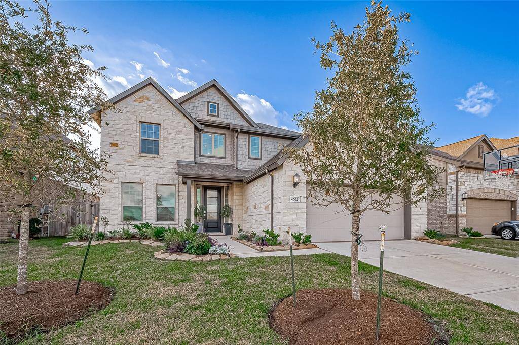 This charming two-story home features a stone exterior, a well-maintained front yard with young trees, and a spacious driveway leading to a double garage. Ideal for family living.