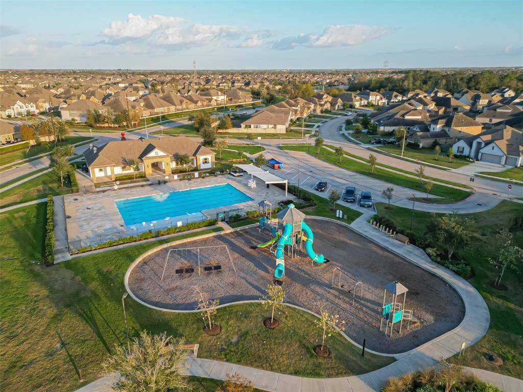 This photo showcases a family-friendly neighborhood featuring a community center with a large swimming pool, a playground, and well-maintained green spaces. The area is surrounded by a network of residential streets with modern homes.