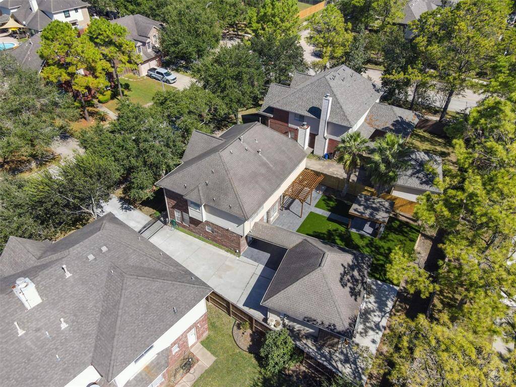 This is an aerial view of a detached, single-family home with a spacious yard, an attached garage, and a mix of developed landscaping and mature trees, located in a suburban neighborhood.