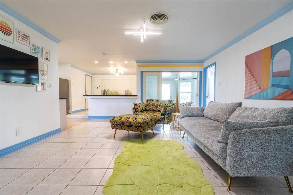 Tiled living room with sunroom in the background to the right and open breakfast area to the left. Crown molding and baseboards. Fourth bedroom to the immediate right is used as home office.