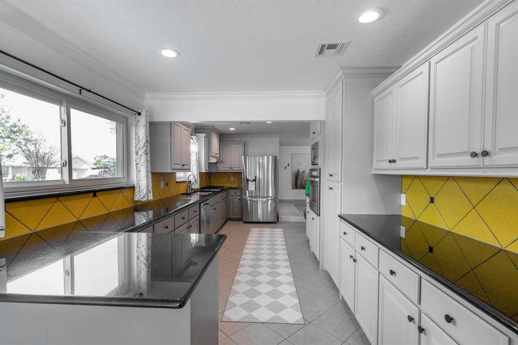 Look at this expansive kitchen! Breakfast bar in the forefront.  Gas cooktop and refrigerator and dishwasher in the background. Breakfast area in the far background with door to utility area and two car garage.