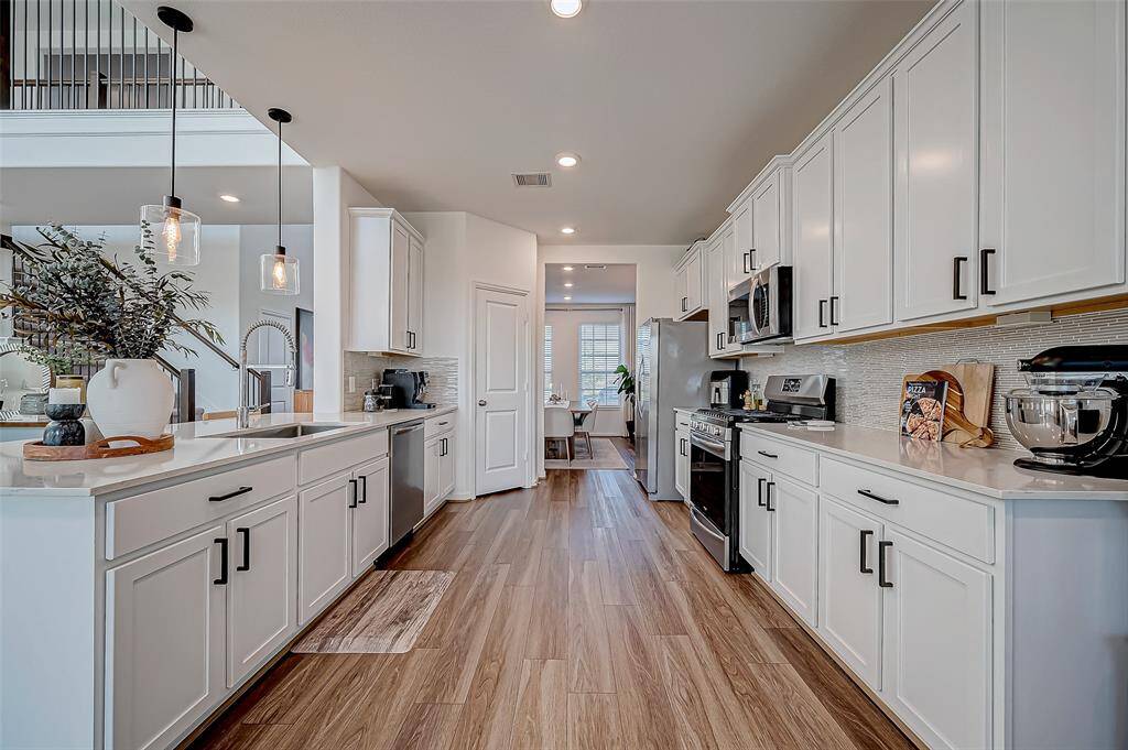This modern kitchen features sleek white cabinetry, stainless steel appliances, and laminate flooring. It offers ample counter space and a bright, open layout, perfect for cooking and entertaining. Refrigerator included.