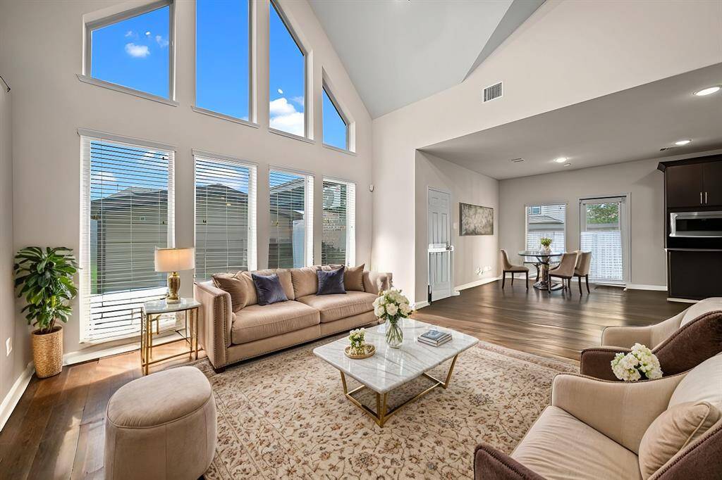 Two story family room with wall of windows, plenty of natural light, and its open to the island kitchen. (Virtually staged)