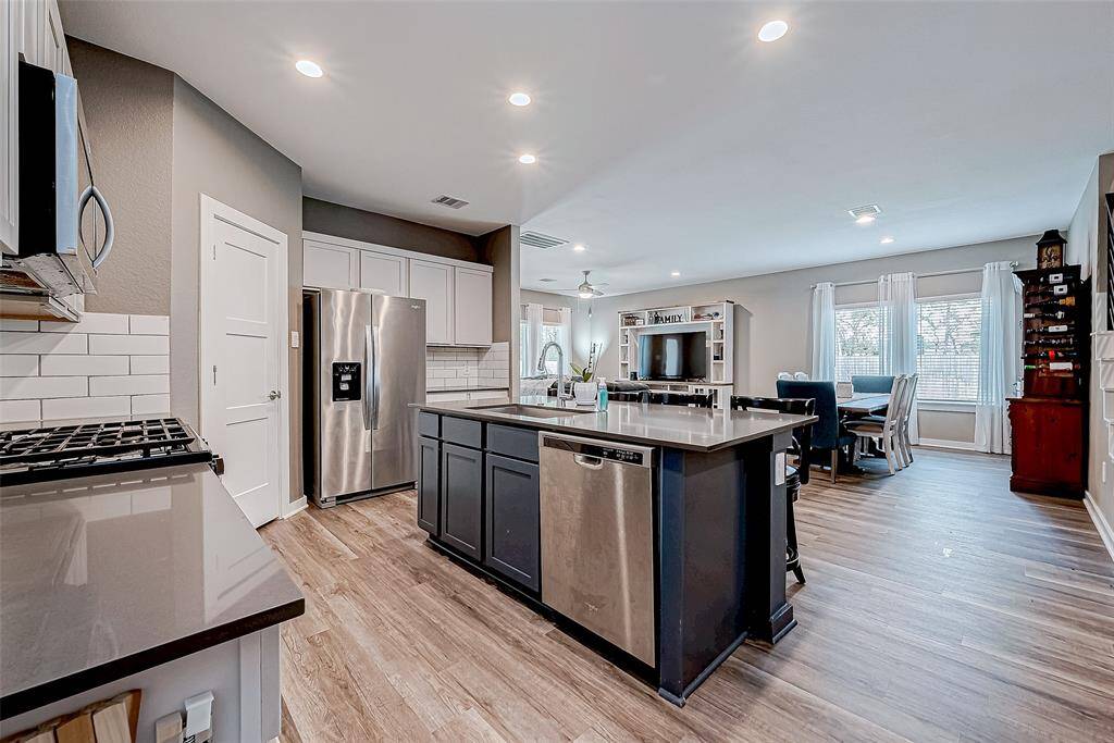 This kitchen boasts quartz countertops, a gas range, subway tile backsplash, a spacious pantry, stainless steel appliances, and a breakfast bar with a large stainless steel sink.