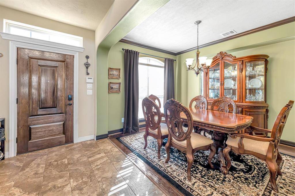 This inviting dining area, adjacent to an elegant wooden front door, features classic furnishings.   Large windows fill the space with natural light, enhancing the tasteful tile flooring and warm color palette.