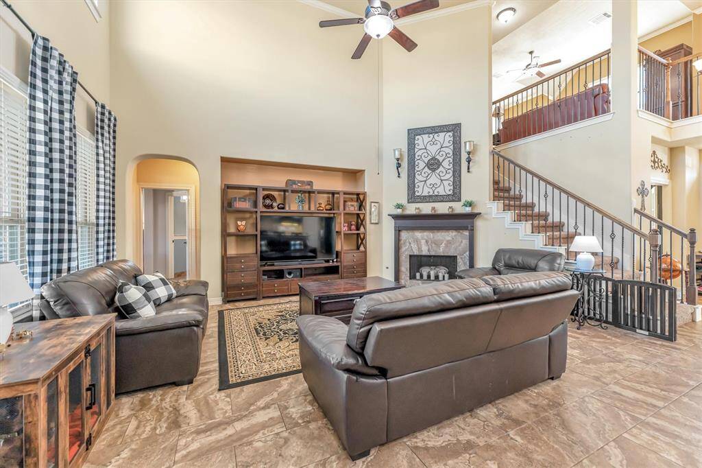 This inviting living room boasts high ceilings, a cozy fireplace, and abundant natural light. Elegant open stairs and a generous living area offer a warm, welcoming ambiance.