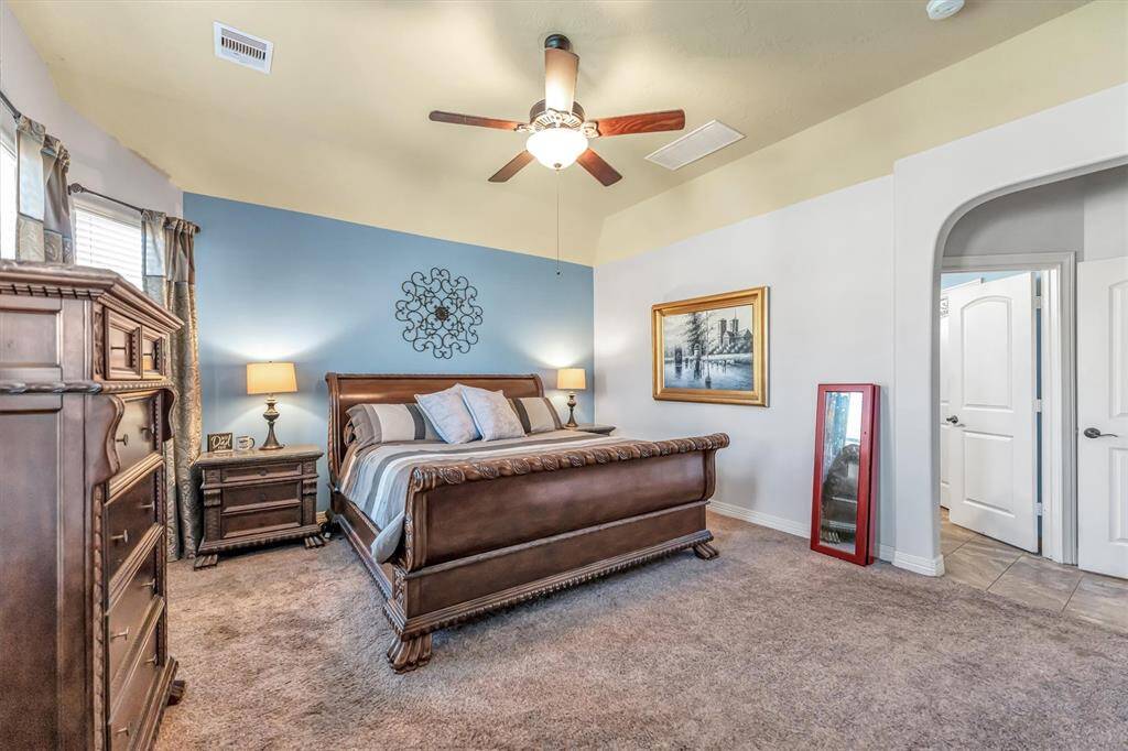 Primary suite offers a spacious retreat with plush carpet, a ceiling fan, and elegant decor.  Soft lighting and a soothing color palette enhance the atmosphere, while an arched doorway leads to an adjacent ensuite area.