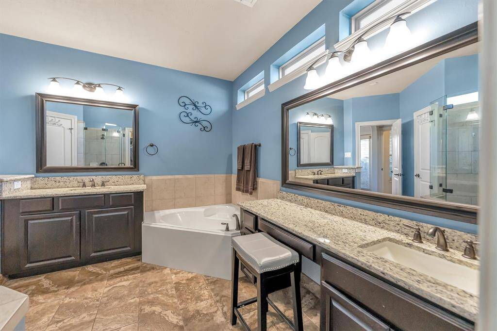Elegant ensuite bathroom boasts a spacious design with dual sinks, granite countertops, and dark wood cabinetry. Enjoy the large soaking tub, separate shower, and calming blue walls that enhance its modern appeal.