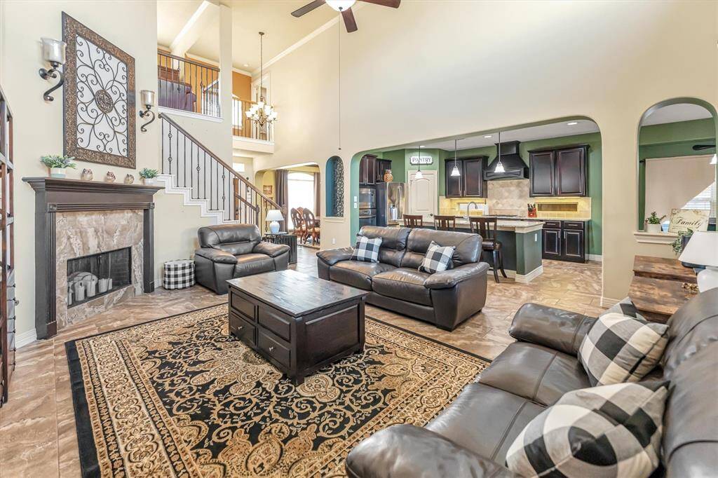 Spacious living area with high ceilings and a cozy fireplace seamlessly connects to a modern kitchen with dark cabinetry, creating the perfect setting for entertaining.