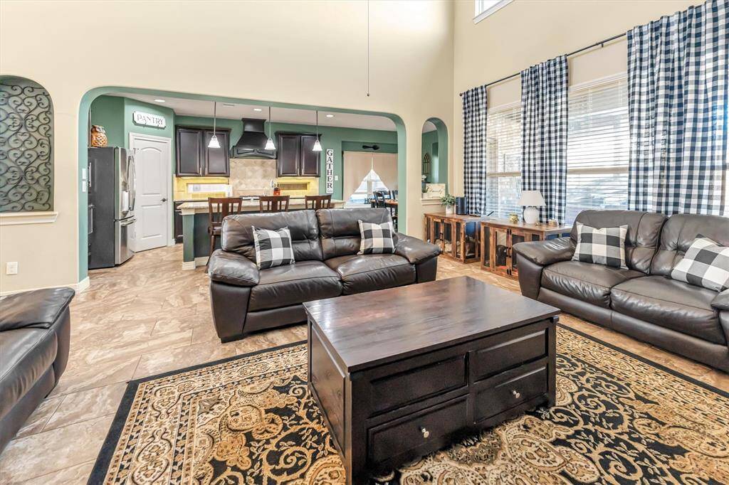 Inviting living area boasts high ceilings, large windows. It seamlessly flows into a modern kitchen with dark cabinetry and a central island, ideal for entertaining.