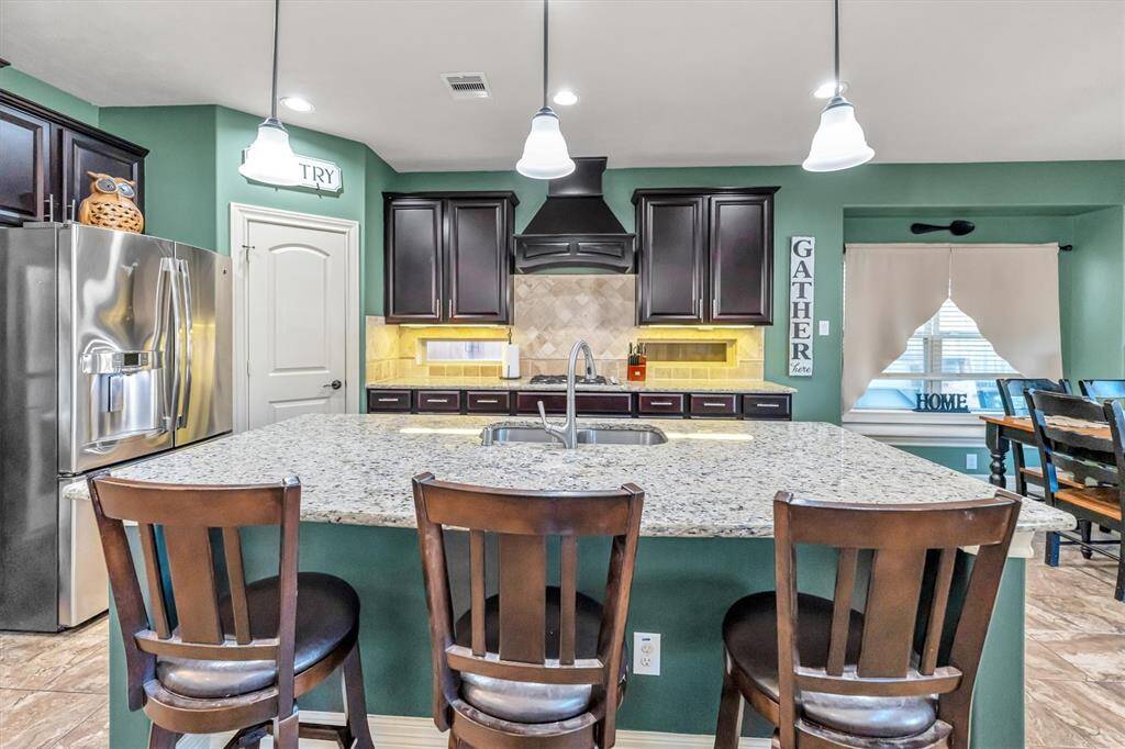 Kitchen boasts a spacious granite island with seating, sleek stainless steel appliances, and elegant dark wood cabinetry, all highlighted by stylish pendant lighting and a cozy dining nook—perfect for gatherings.