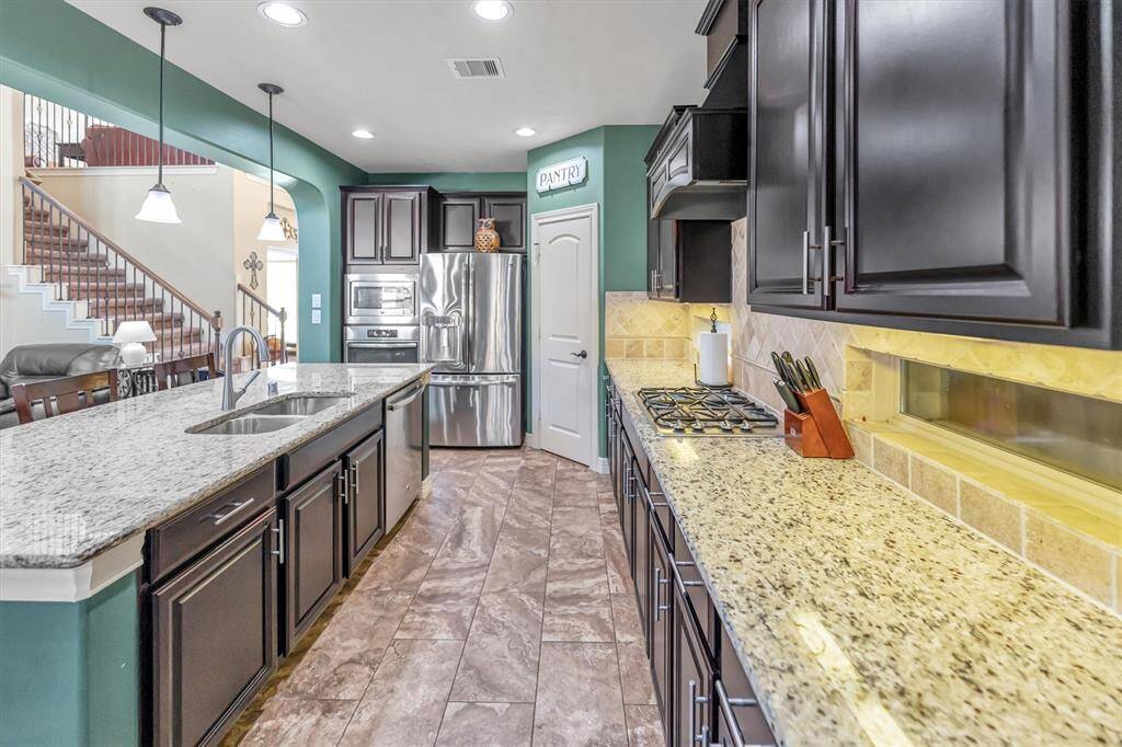 Modern kitchen boasts granite countertops, stainless steel appliances, and rich dark wood cabinetry. Its spacious layout includes a large island, stylish pendant lighting, and a cozy dining nook—perfect for entertaining. gatherings.