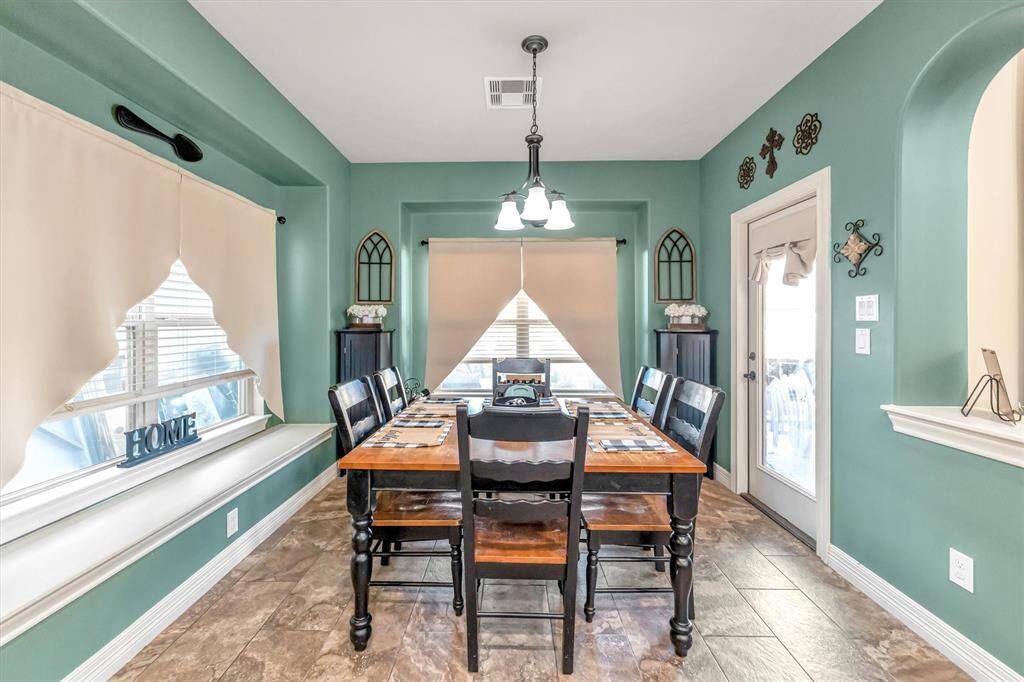Cozy dining area with abundant natural light, featuring stylish decor, a chic light fixture, and convenient outdoor access through a glass door to the outdoor living area and pool.